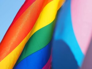Foto da bandeira LGBTI em movimento, junto com a bandeira trans